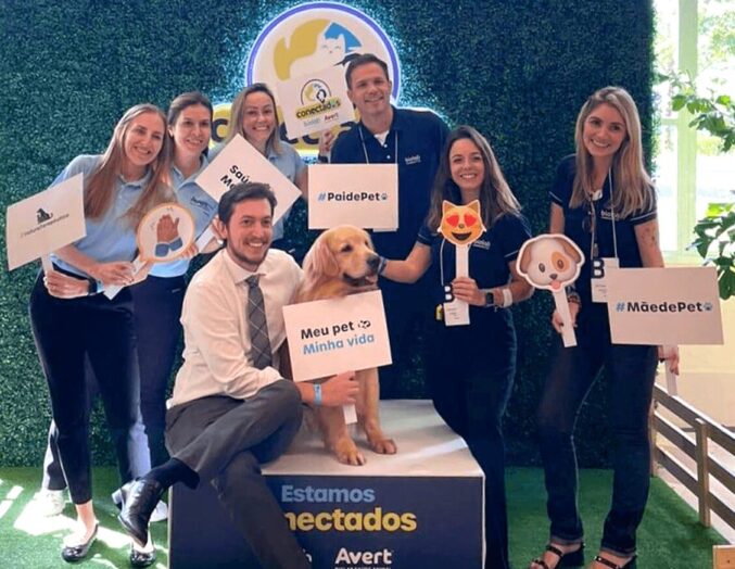 A photo of a group of people with a golden dog, standing on a platform with the words Estamo conectados, Biolab and Avert logos below. Each person in the group is holding a sign with a different phrase on it.