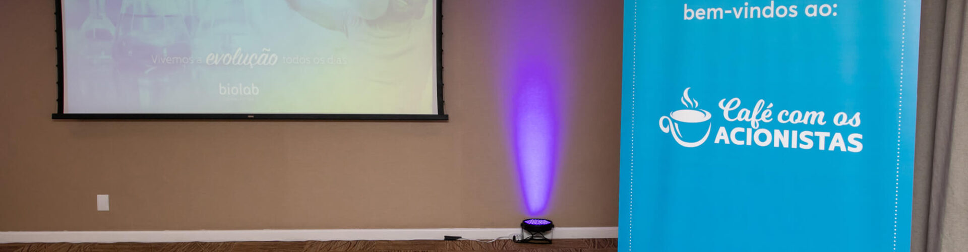 Banner with the Coffee with Shareholders event logo and in the background, a projection screen set up to show a presentation